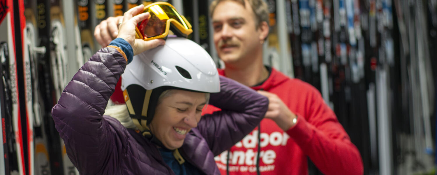 person is assisted in trying on ski goggles over helmet