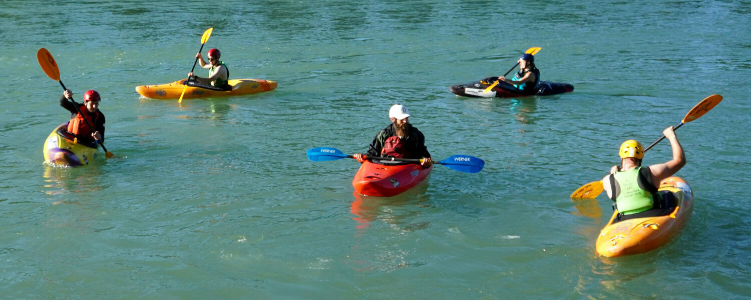 five kayakers paddle on calm river eddy