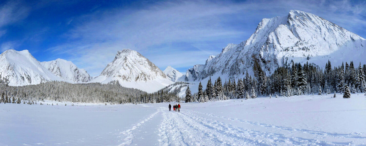 snowshoers in open meadow beneath ring of mountains