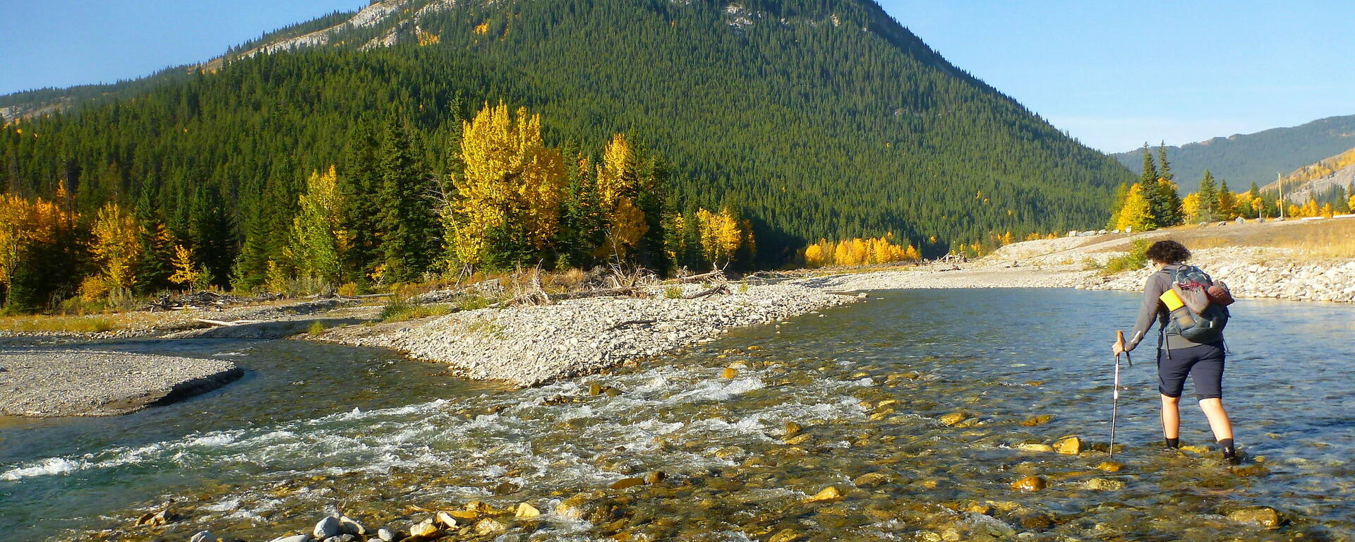 hiker walks across a low-flowing river