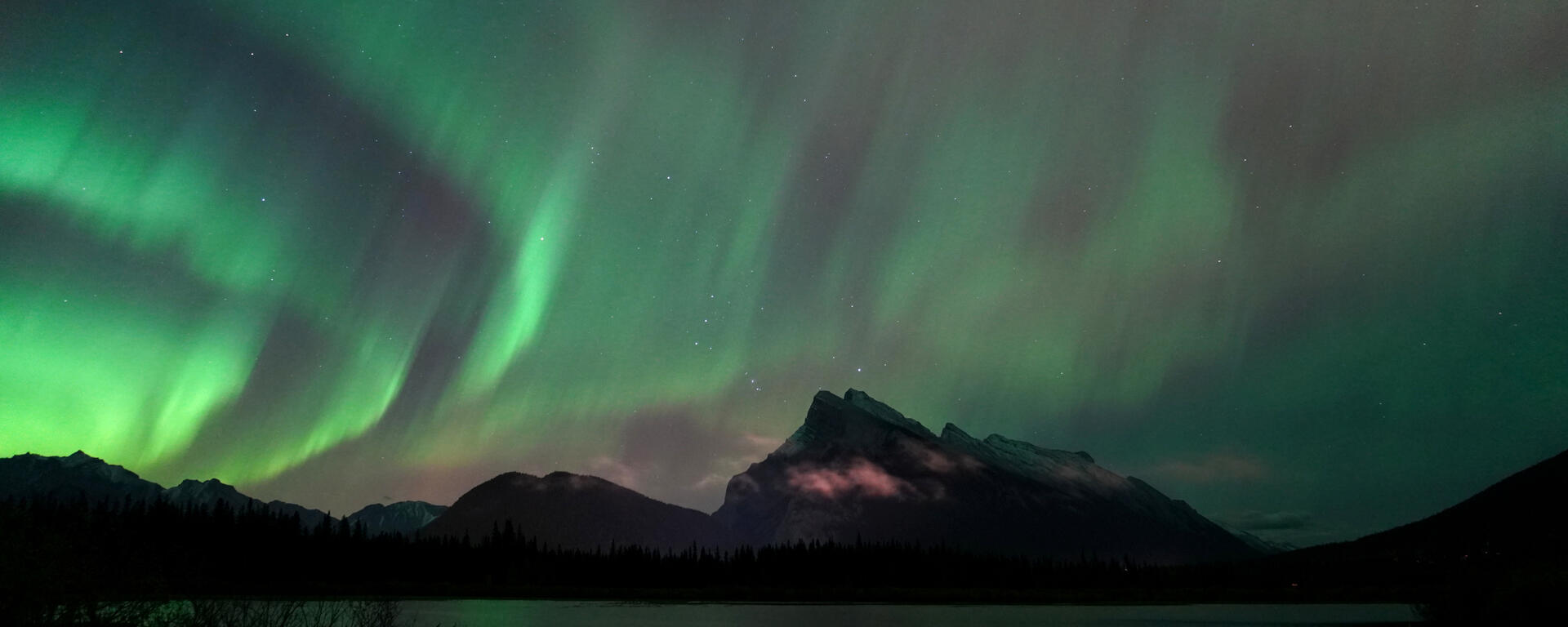 green arcs of aurora over Mount Rundle with low clouds