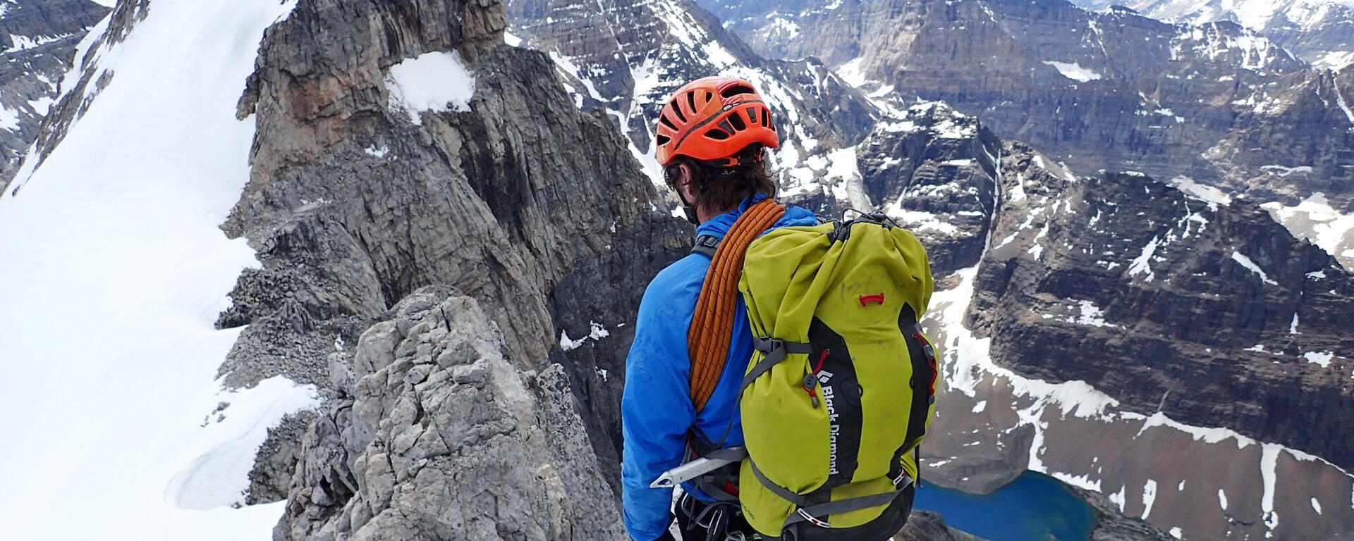 mountaineer wearing backpack and helmet looks out along ridge and mountain vista