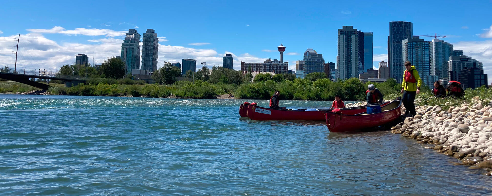 canoes on the shore of the Bow River with Calgary downtown behind