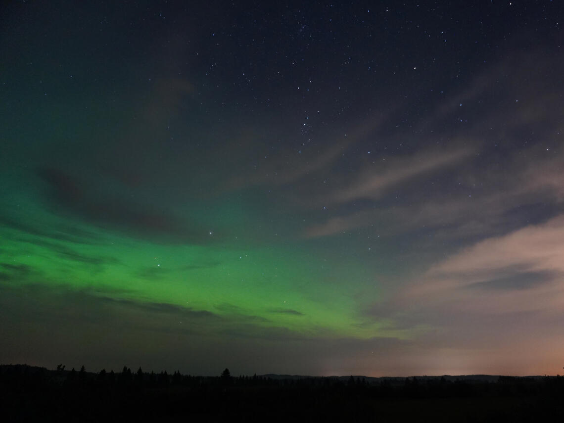 green aurora glow and stars behind light clouds