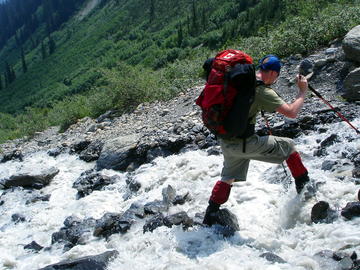 backpacker crosses rocky stream with the help of trekking poles