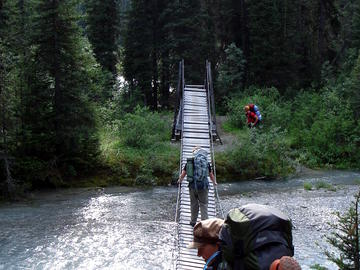 backpackers cross suspension bridge over milky blue river