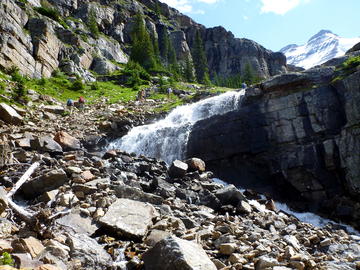 hikers ascend rocky trail beside waterfall with talus in foreground