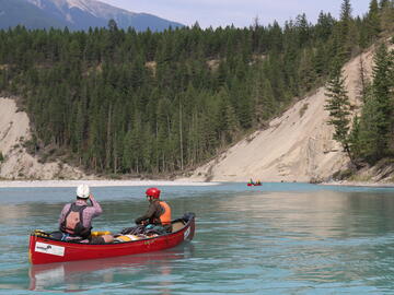 canoe on turquoise water below hillside