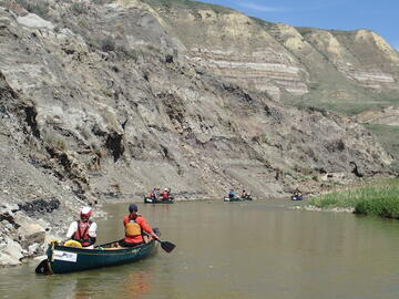 canoe on calm river below badland hills