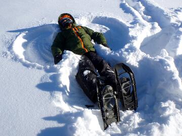 child making snow angel while wearing puffy clothes and snowshoes