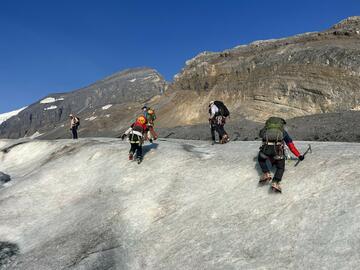 five people ascent band of ice with rock cliff behind