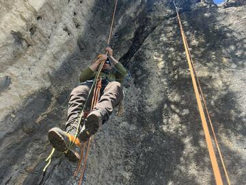 ropes hang from cliff with man ascending rope using tools and rope steps