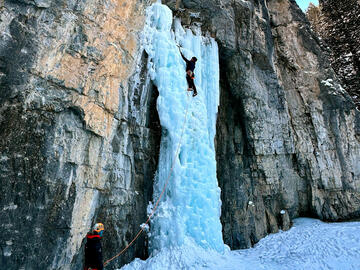 one person belays another climbing ice fall