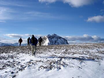 group walks across a snowy, rocky plateau toward mountain