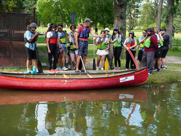 people listen on shore with canoe in water foreground