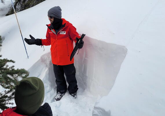 instructor standing before test pit in snow