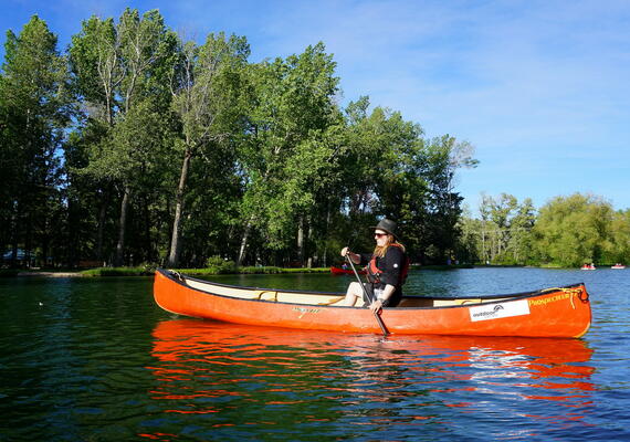 man paddles a canoe on calm lagoon with trees behind