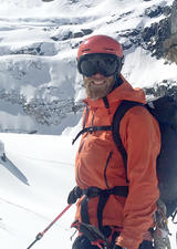 Brad in helmet and ski goggles in front of snowy mountains